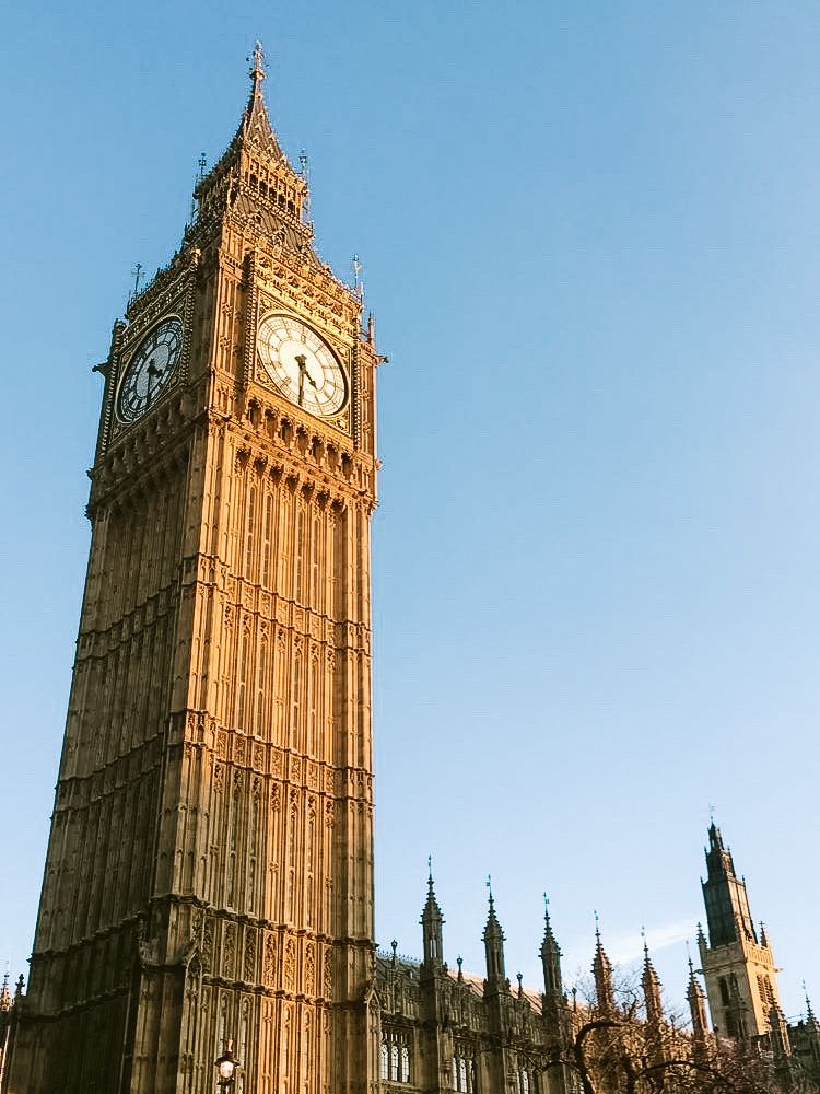 The iconic Big Ben clock tower glowing in warm sunlight against a clear blue sky.