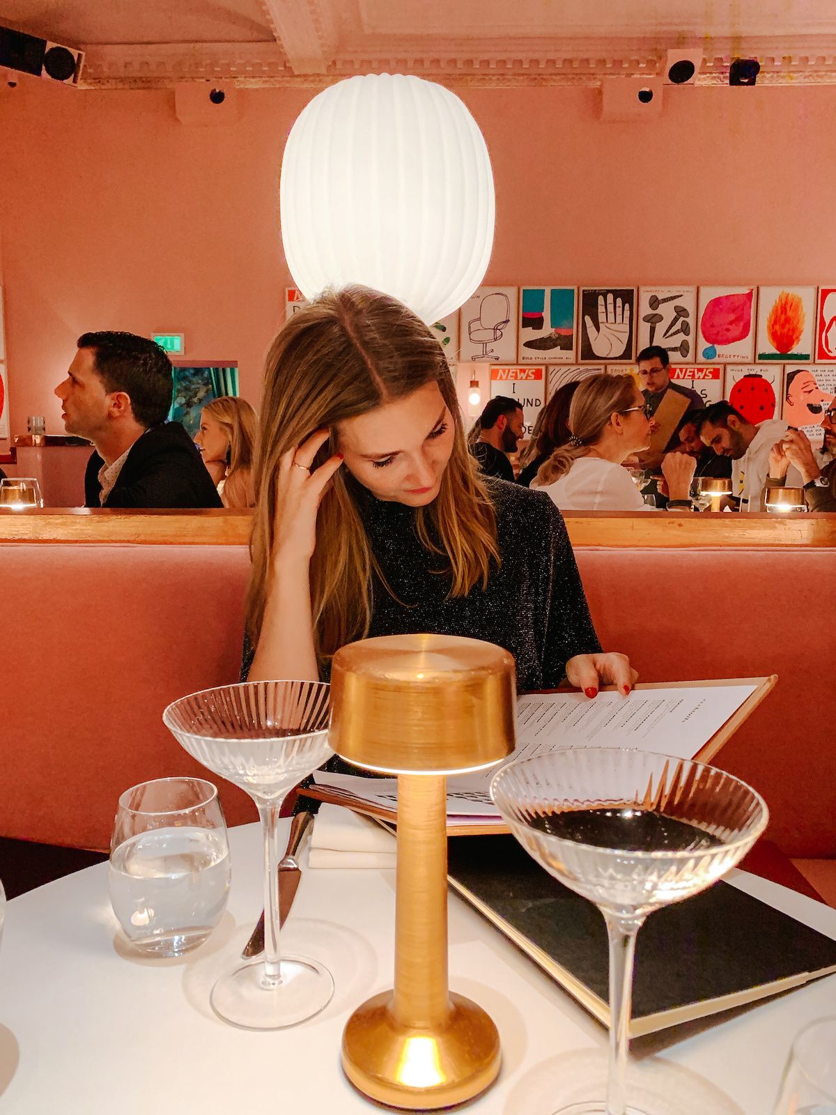 Cec reading the menu at The Gallery in Sketch, a stylish restaurant with pink velvet seating and quirky wall art.