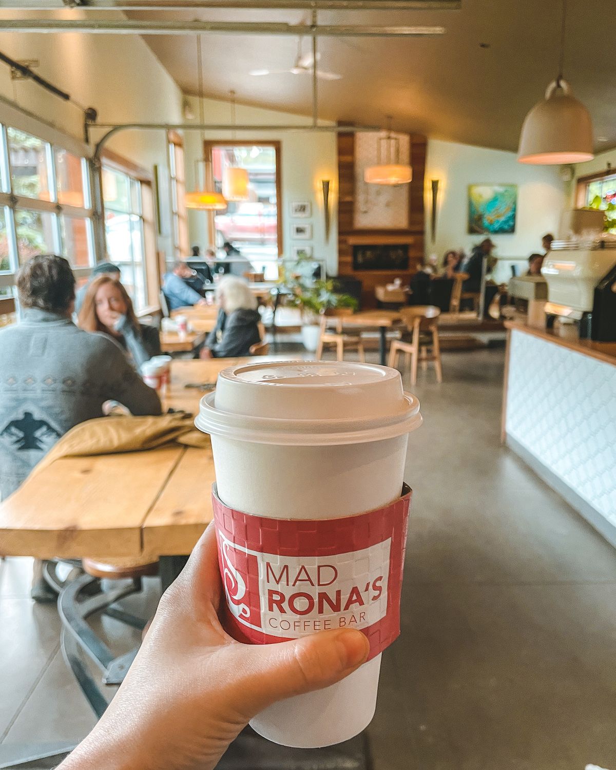 Coffee being held by hand with Mad Rona's interior in background