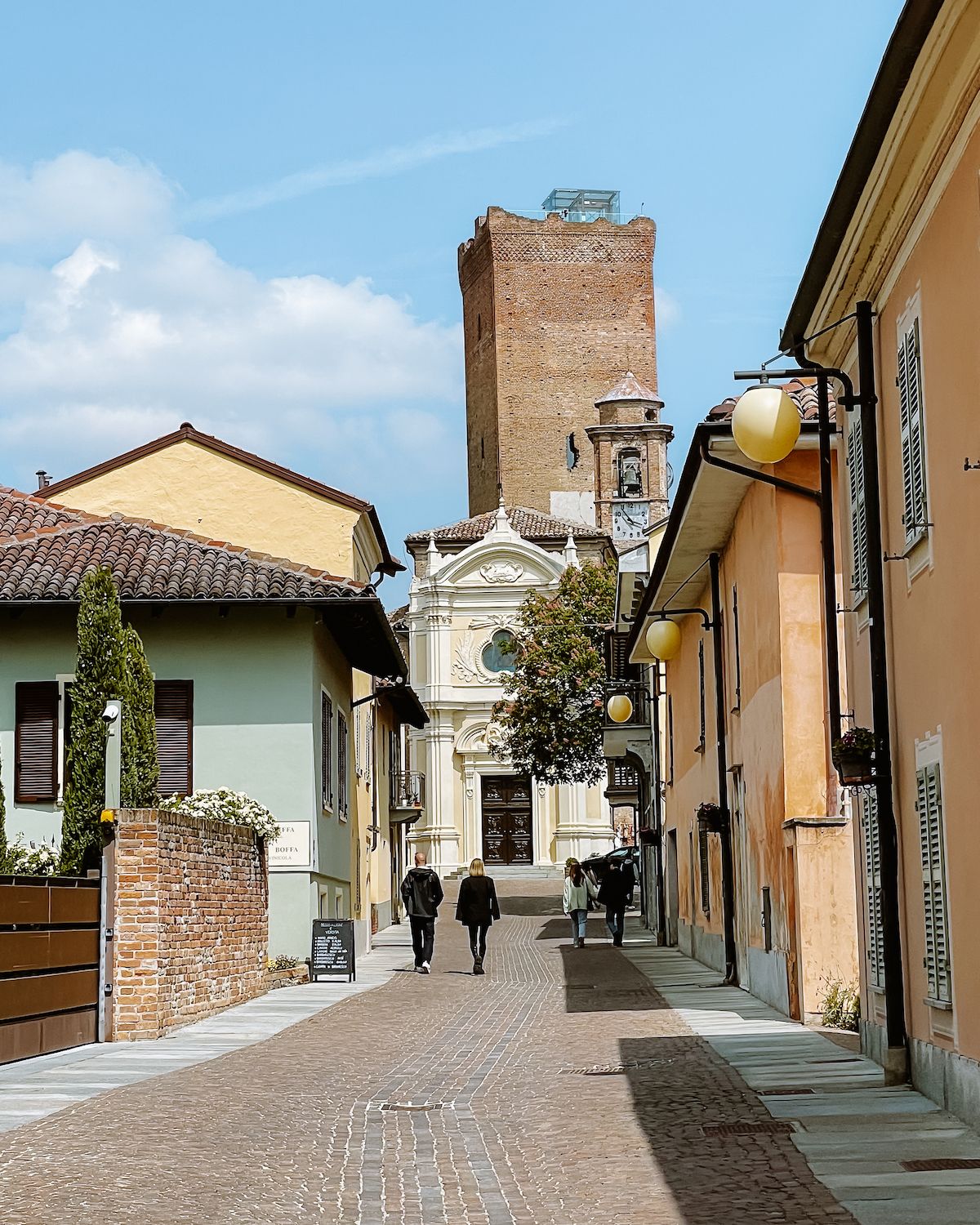 People walking on a cobblestone street in Barbaresco towards a medieval siege tower