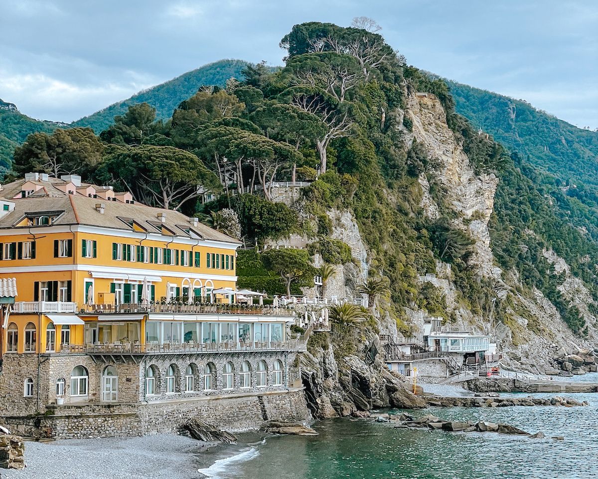 Yellow beachfront resort in Camogli with rocky green cliffs behind it