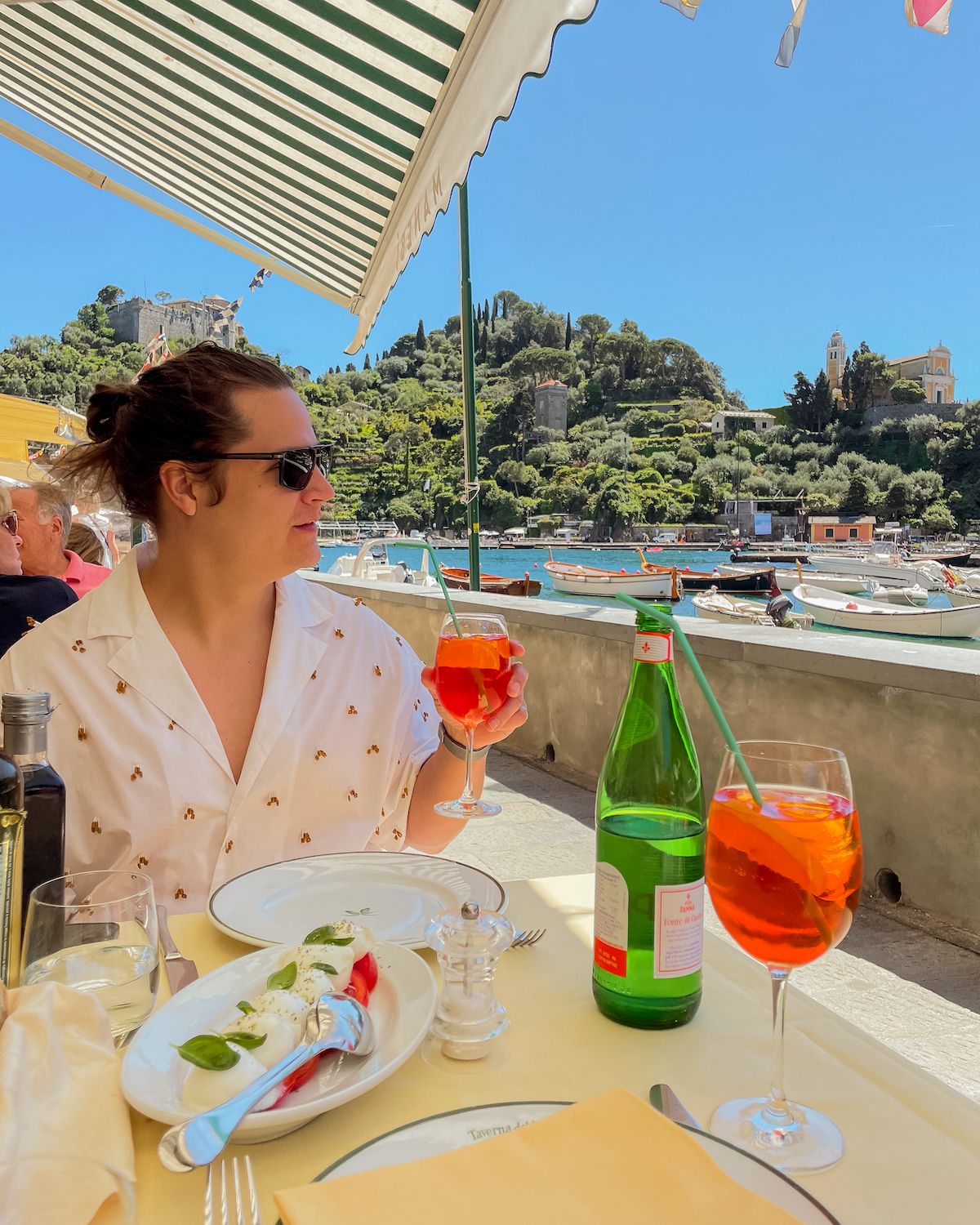 Man with white shirt drinking an Aperol Spritz at an outside table along the Portofino harbourfront 