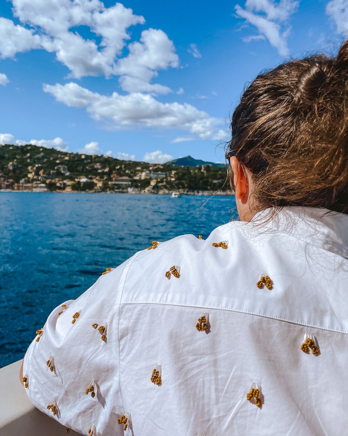 Man in white shirt with yellow beadwork in a boat looking out onto the blue Ligurian Sea