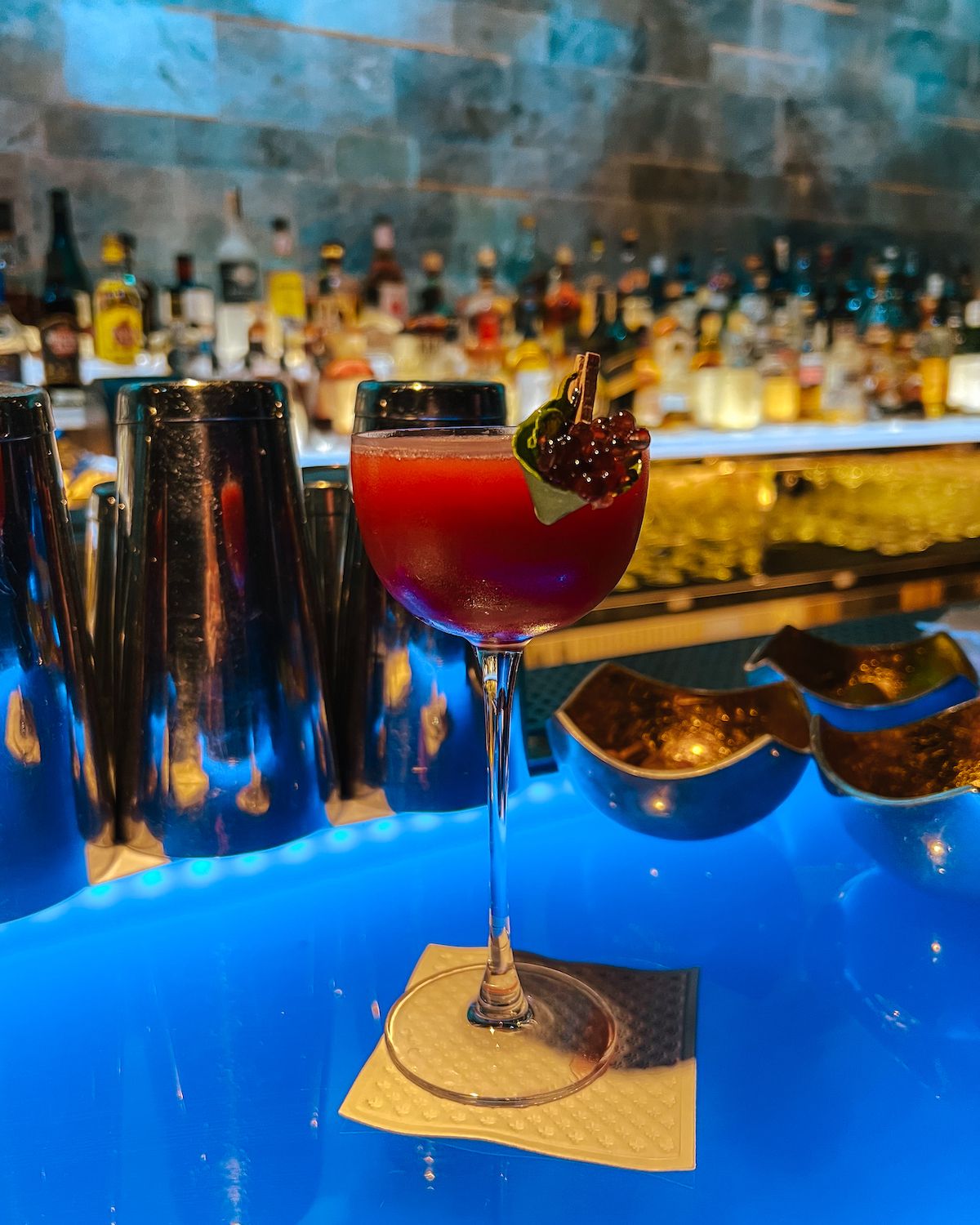 Red cocktail in a coupe glass on a blue bar table