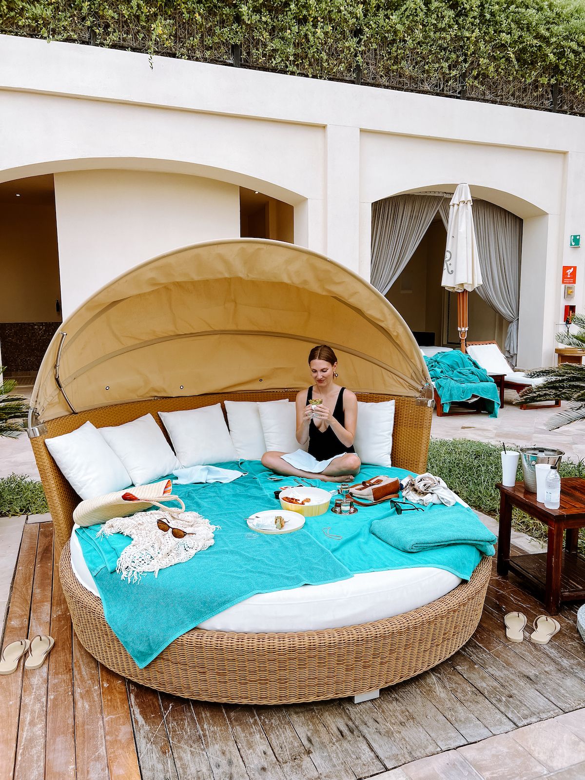 Blonde girl in black bathing suit sitting on a cabana chair with poolside bites