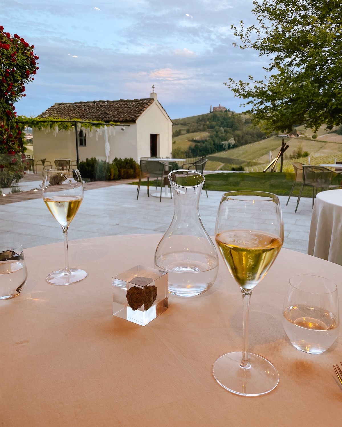 Two wine glasses with prosecco overlooking a small white church and Barolo vineyards