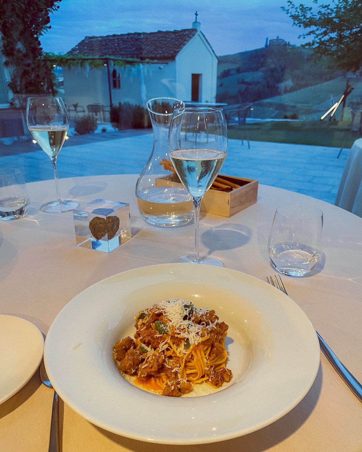 Spaghetti bolognese on a table with views small white church and a Barolo vineyard at dusk