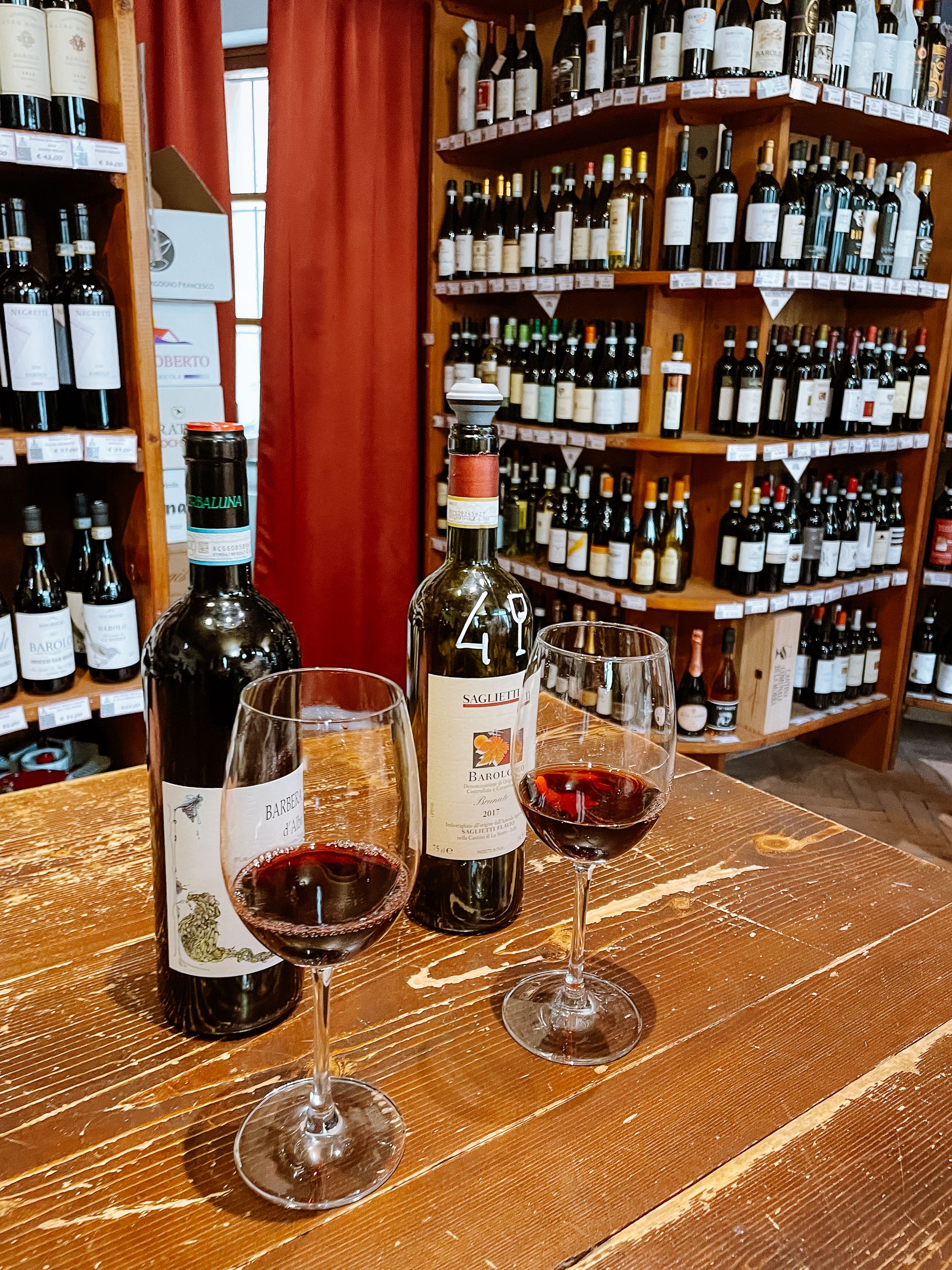 Two glasses of red wine in front of their corresponding bottles in a wine shop