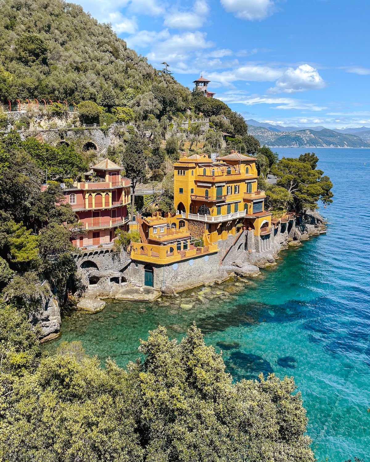 Pastel pink and yellow coloured buildings perched over a turquoise cove near Portofino
