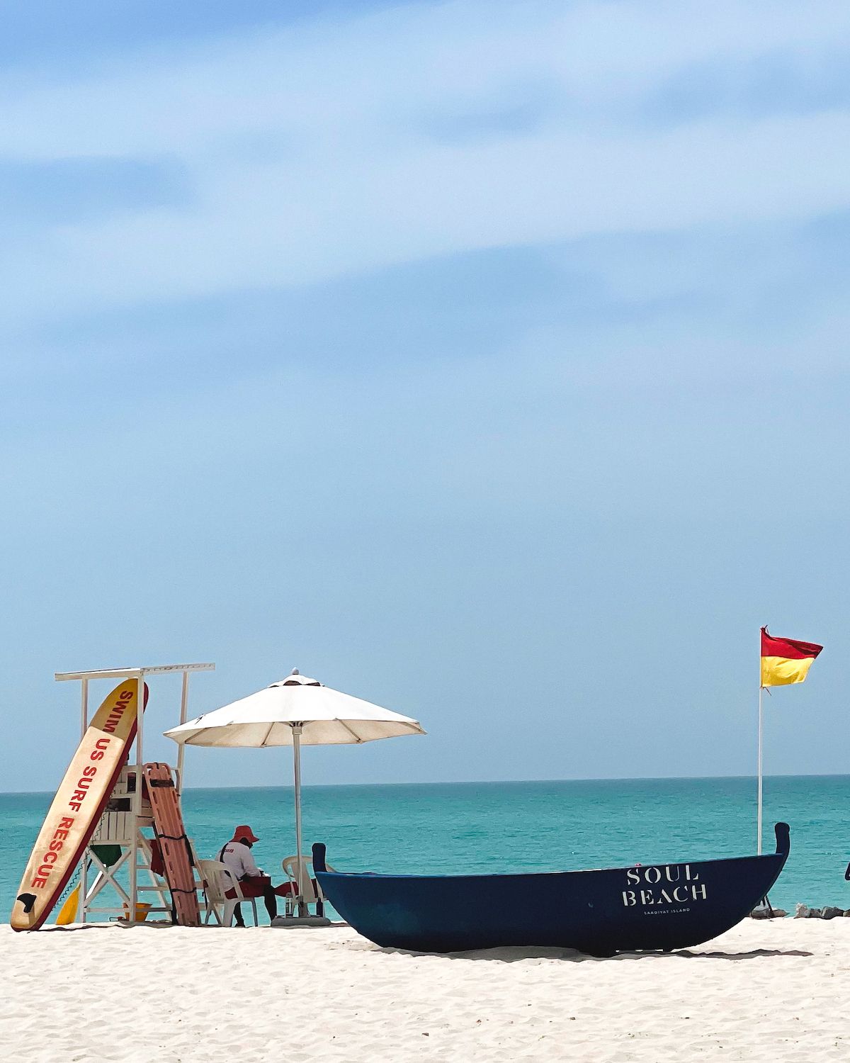 Blue boat in sand and lifeguard under a white umbrella on Soul Beach in Abu Dhabi