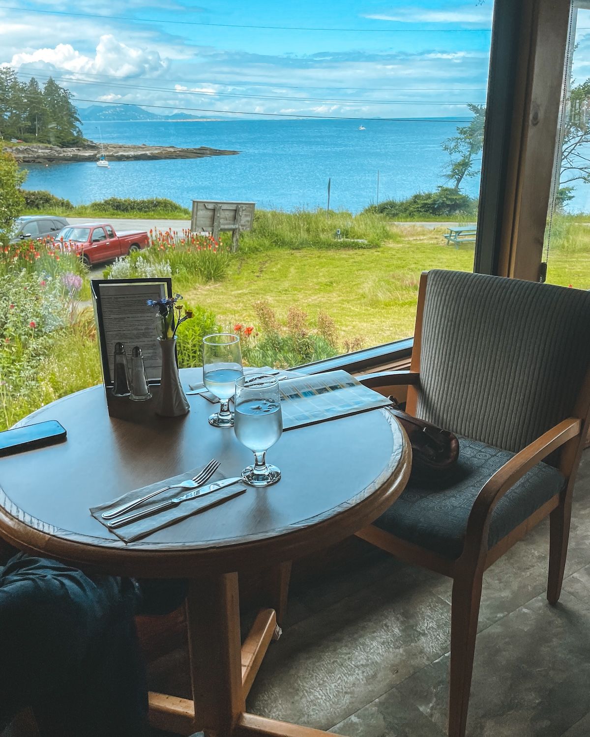 Round table and chair against a window with green grass and the ocean as the backdrop at the Surf Lodge dining room