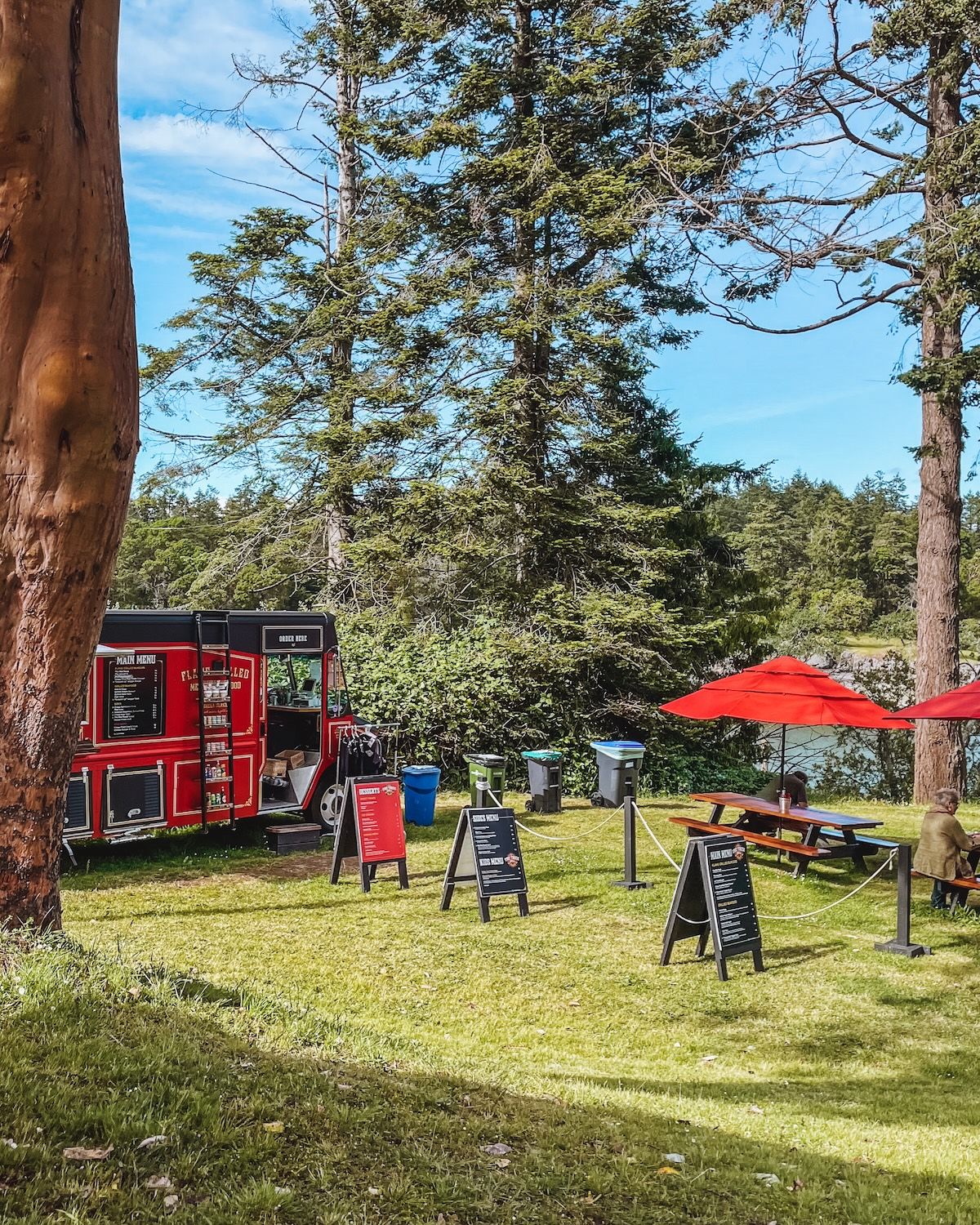The red Fireside food truck parked in a grassy lawn with picnic tables and red umbrellas