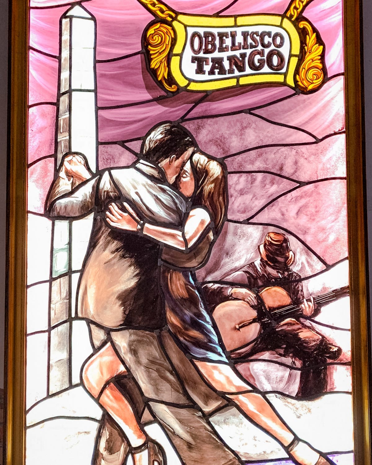 Stained glass artwork of a couple dancing tango in front of the Obelisco, with a guitarist playing in the background.