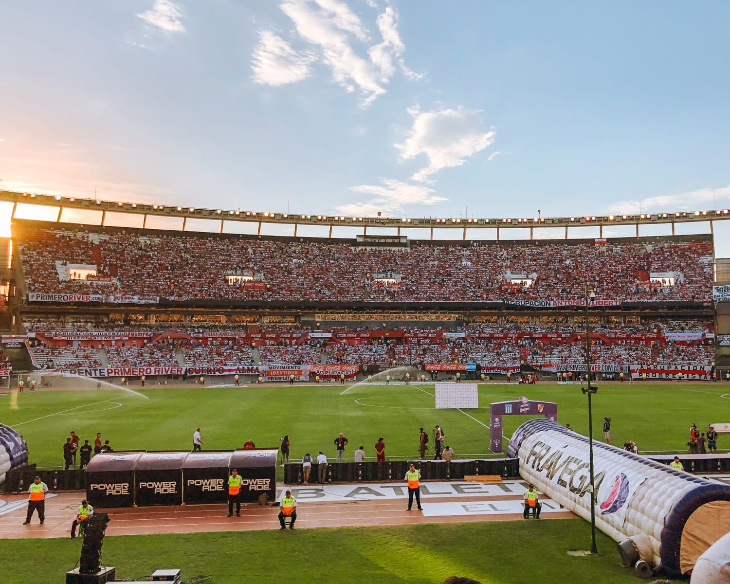 Panoramic view of Monumental Stadium at sunset, with a sea of fans and banners filling the stands before kickoff.