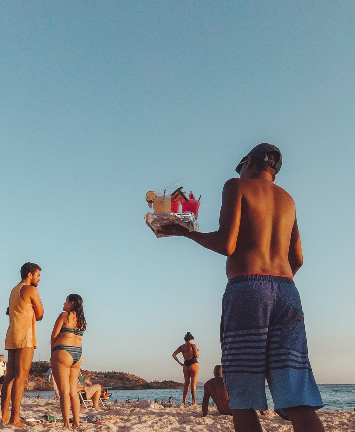 A vendor on Ipanema Beach holding a tray of colourful drinks.