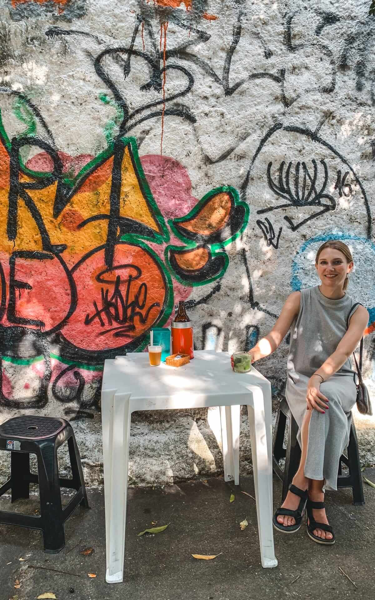 Cec enjoying drinks at a plastic table set against a graffiti-covered wall at Bar do Serginho, a fun and casual neighbourhood bar in Santa Teresa.