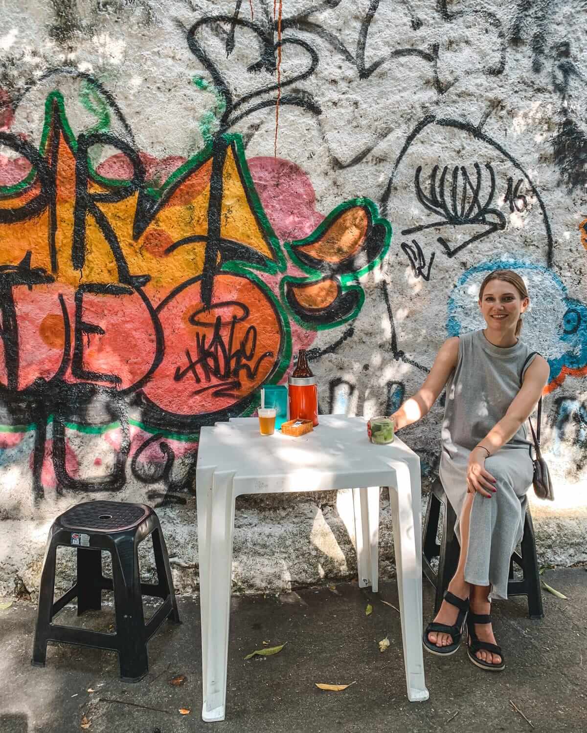 Cec sitting at a white plastic table with drinks beside a graffiti-covered wall, in the artsy Santa Teresa neighbourhood.