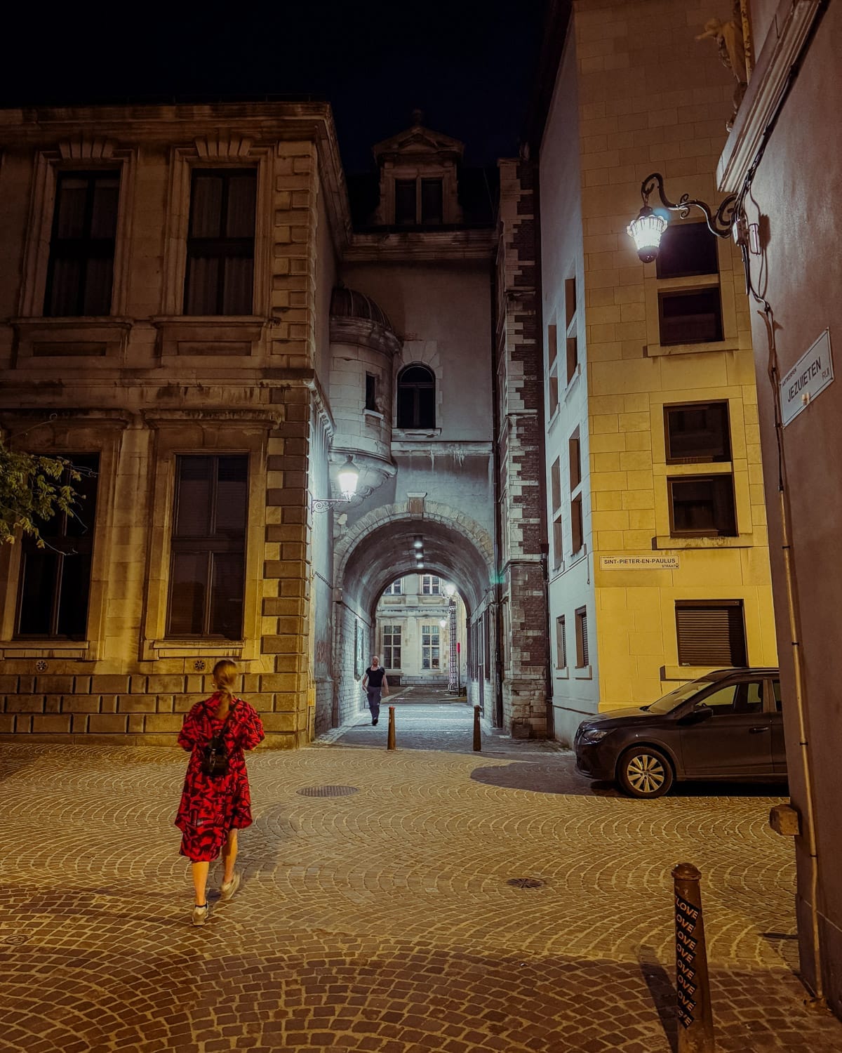 Cec walking through a softly lit cobblestone alley framed by historic buildings in Antwerp at night.