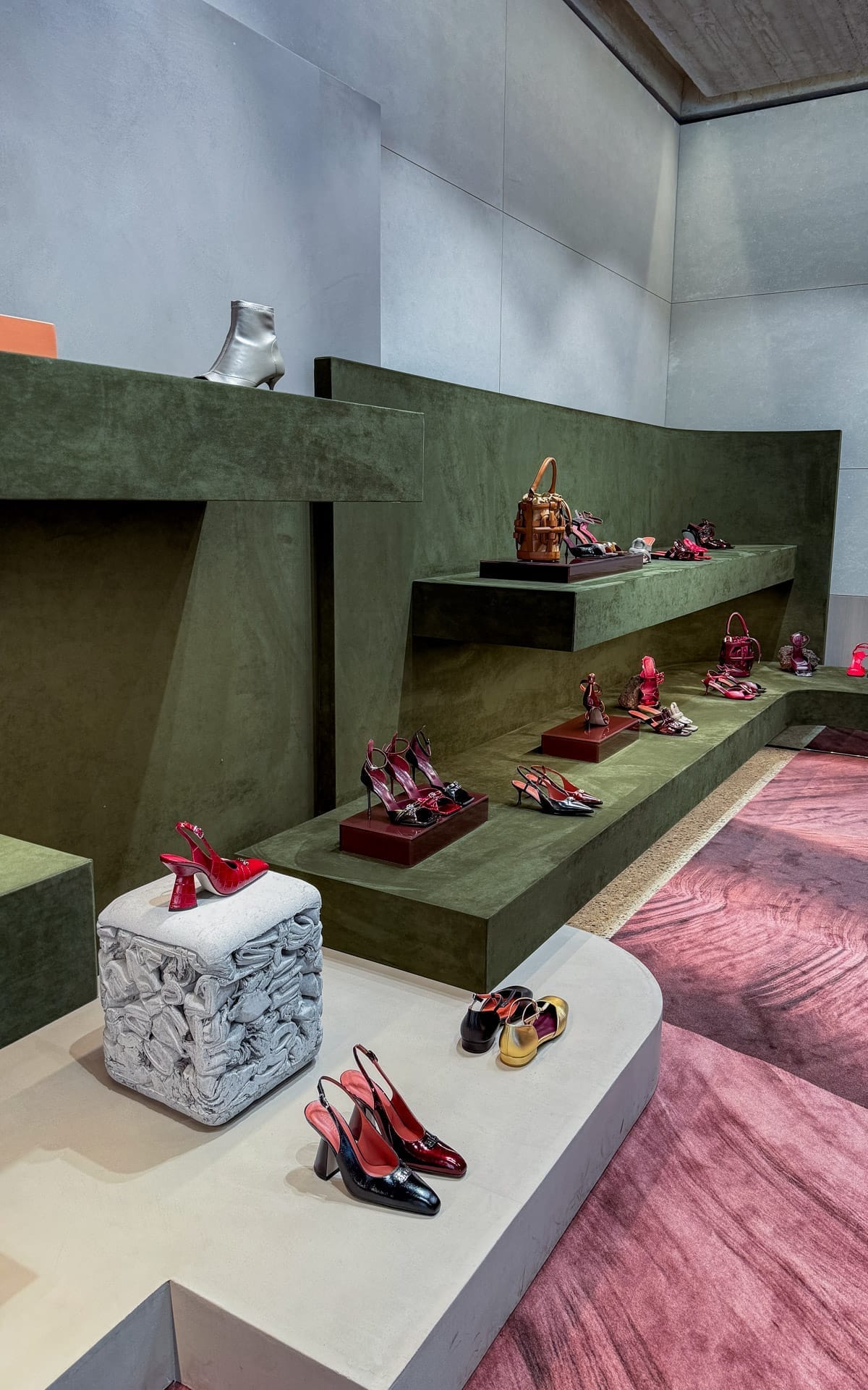 Designer shoes and handbags arranged on modern olive-toned geometric shelves at Morobe in Antwerp.