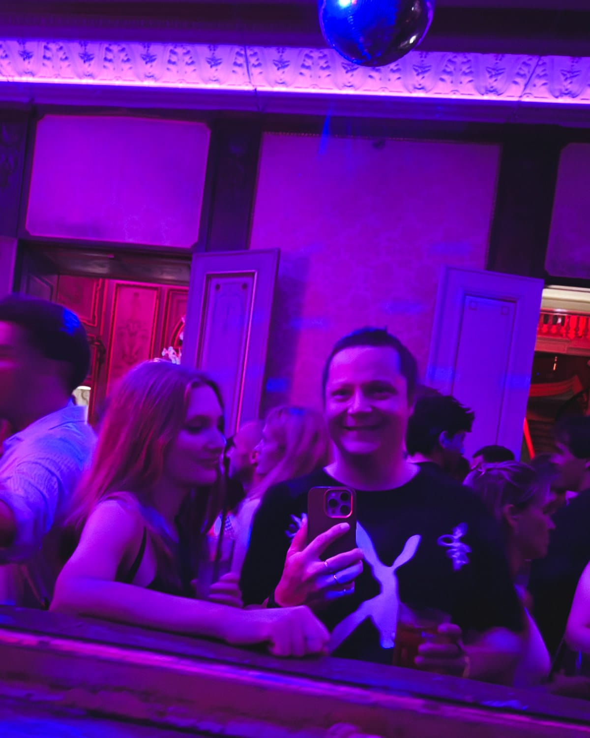 Group selfie taken in a lively, neon-lit nightclub in Antwerp with purple and pink lighting under a disco ball.
