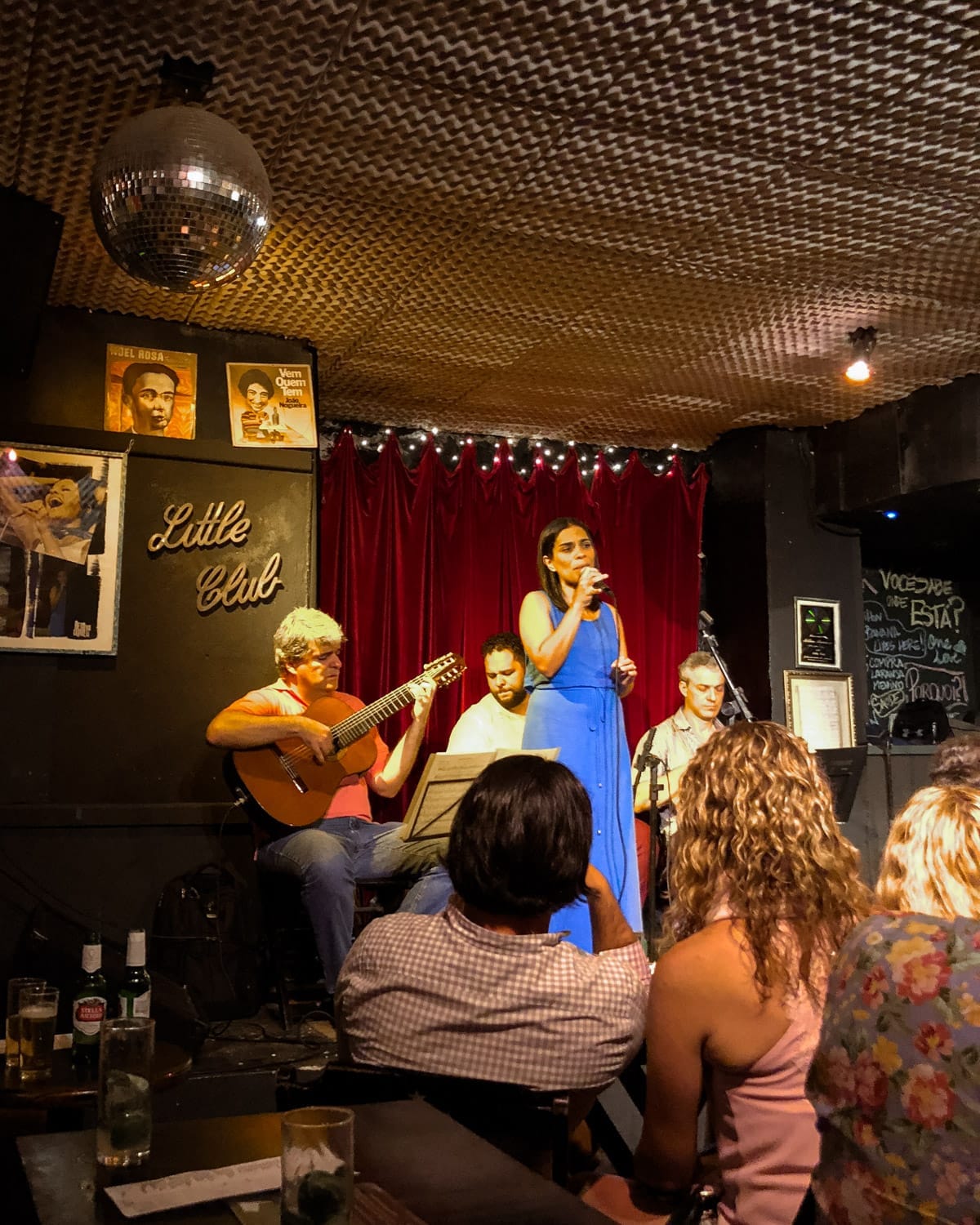 Flavia Dantes in a blue dress performs live bossa nova with a small acoustic band on stage in Little Club at Beco Das Garrafas.