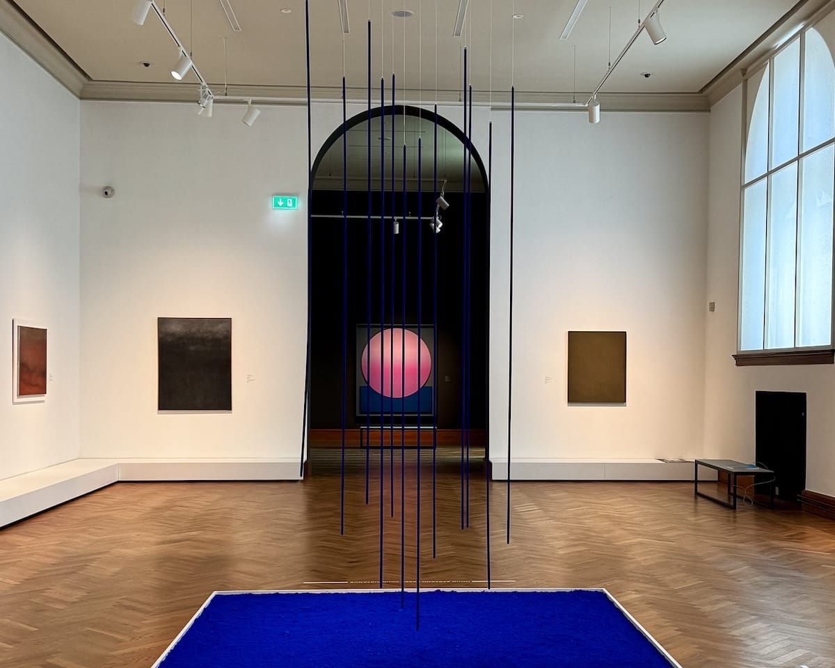 Gallery room at KMSKA with Jef Verheyen artworks and vertical blue rods suspended over a vivid blue square installation on the floor.