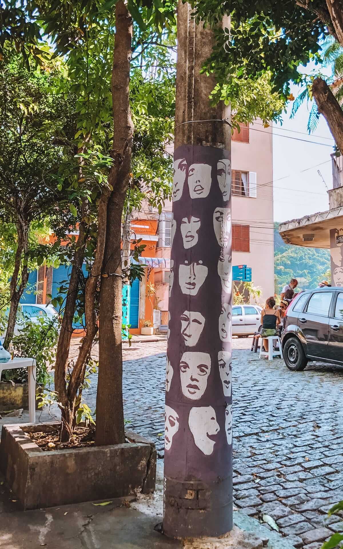 A painted utility pole featuring expressive faces, captured on a cobblestone street in Santa Teresa, one of the most Instagrammable neighbourhoods in Rio de Janeiro.