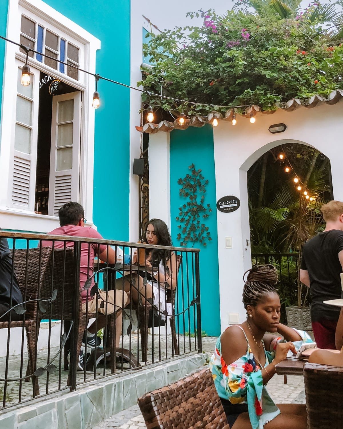 People dining and drinking on a colourful patio with turquoise walls and hanging string lights at Explorer Bar, one of the best bars for cocktails in Rio.