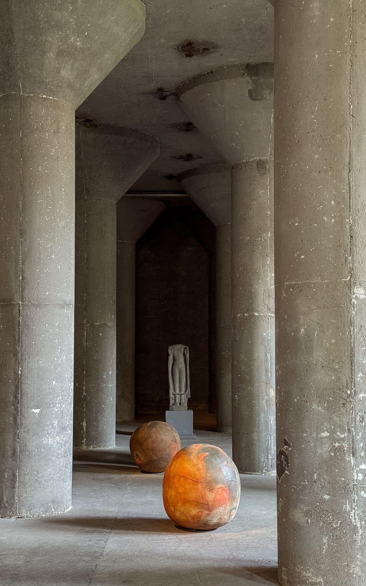 Industrial-style gallery featuring massive concrete columns, two glowing ceramic spheres, and a headless statue in the distance at Kaanal gallery.
