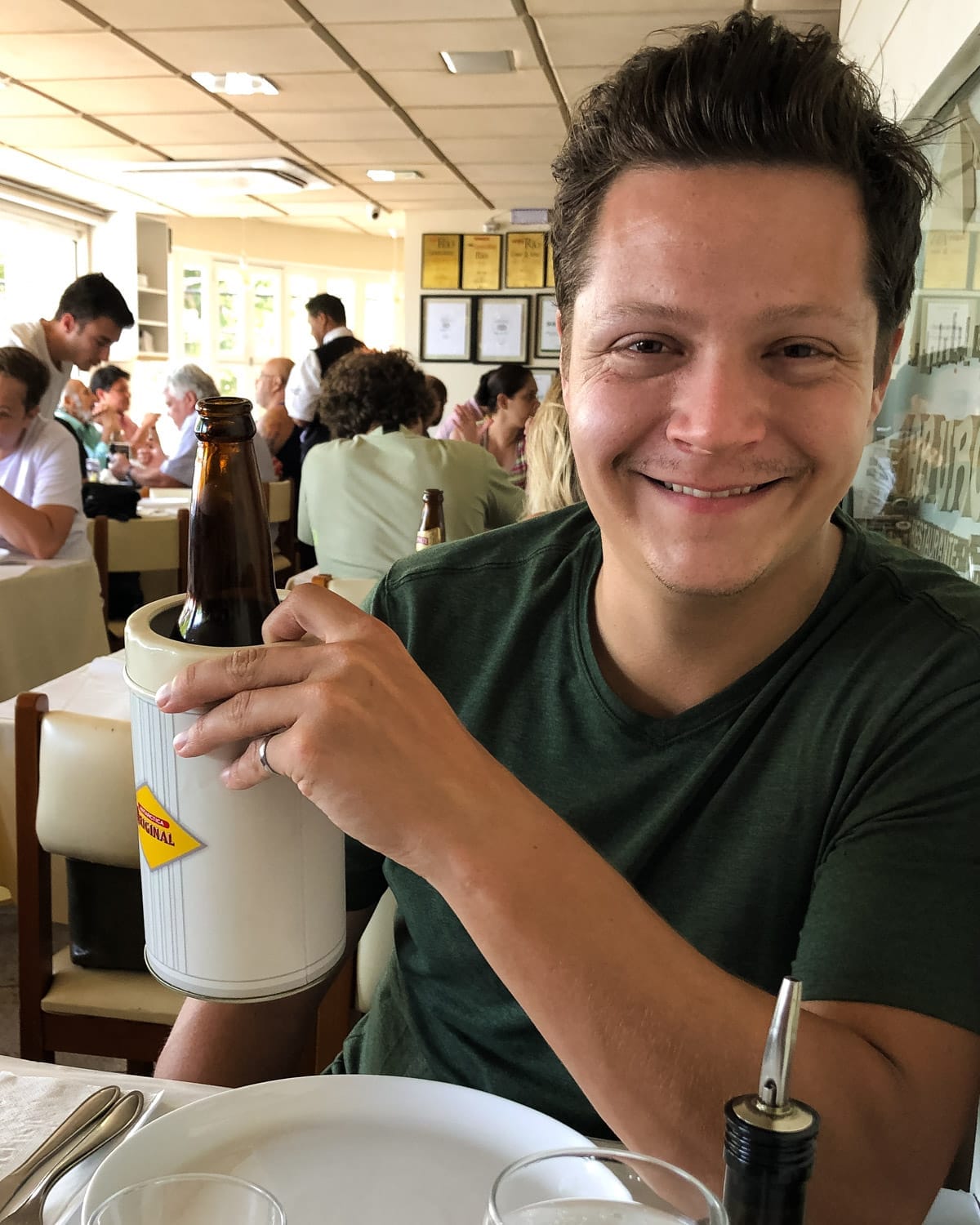 Ari smiling inside a lively local restaurant in Rio De Janeiro holding an ice-cold beer in a chiller.