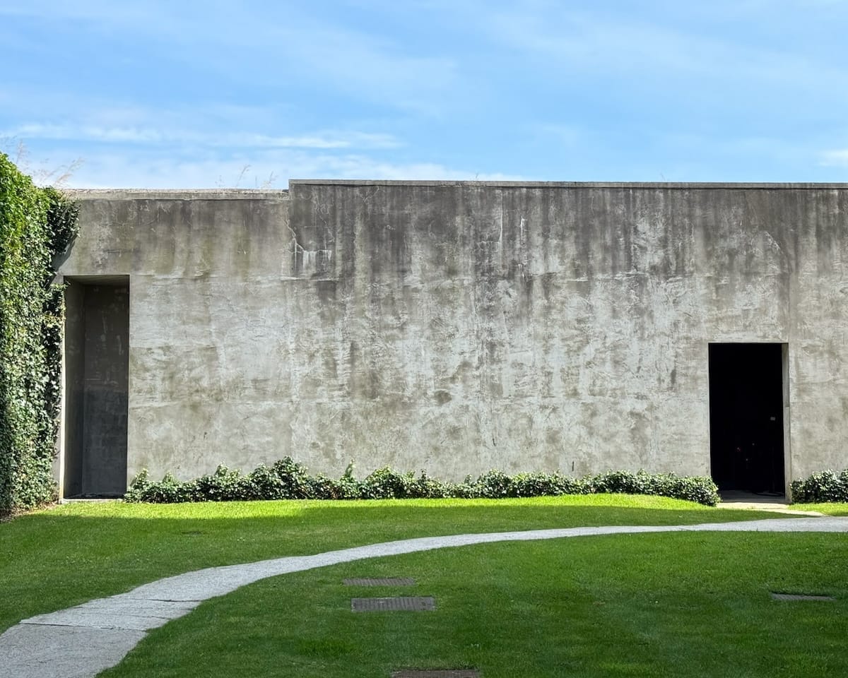Exterior of Axel Vervoordt’s art gallery, Kanaal, just outside of Antwerp, with ivy-covered walls, rough concrete facade, and a winding stone path cutting through green grass.