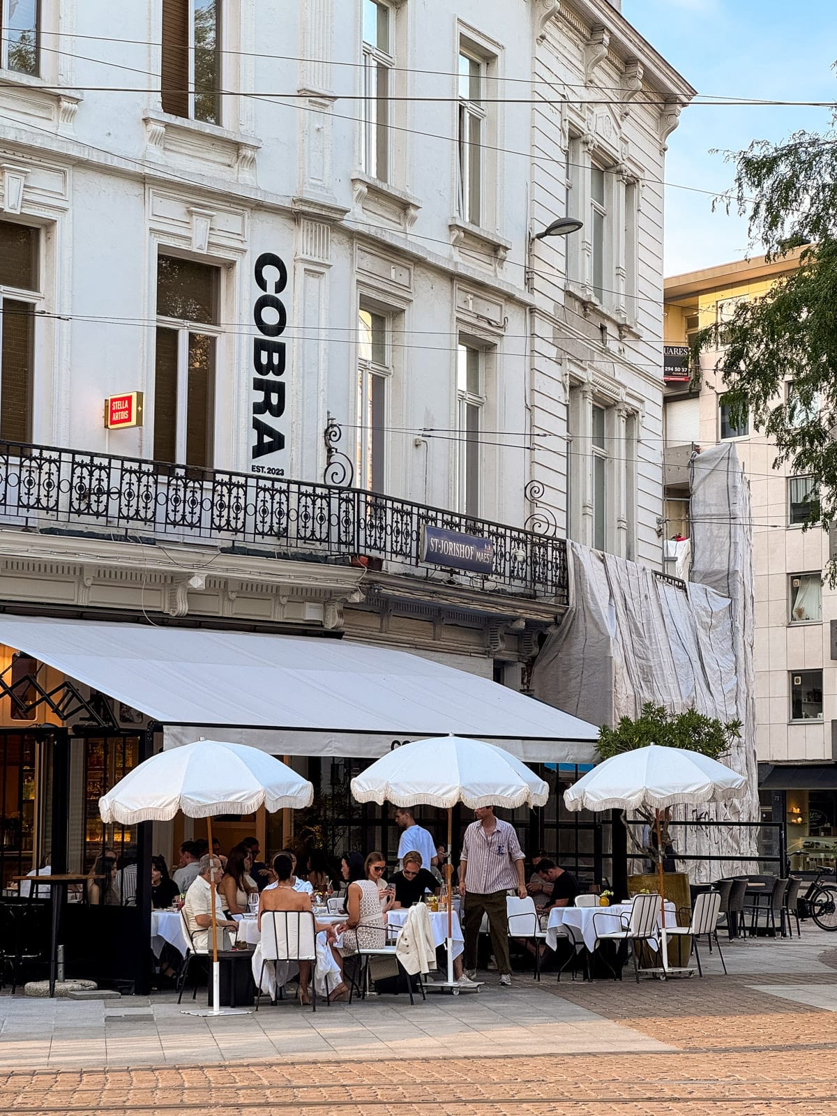 Diners sit under white umbrellas outside Cobra restaurant, housed in a classic white building.