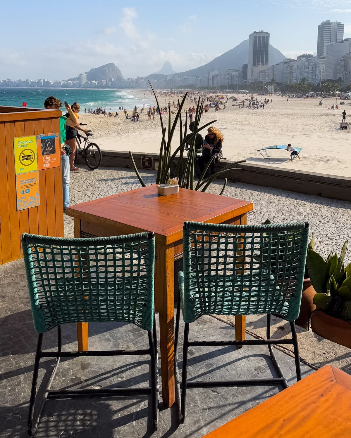 Two teal woven chairs at Quiosque Mureta do Leme facing Copacabana Beach.