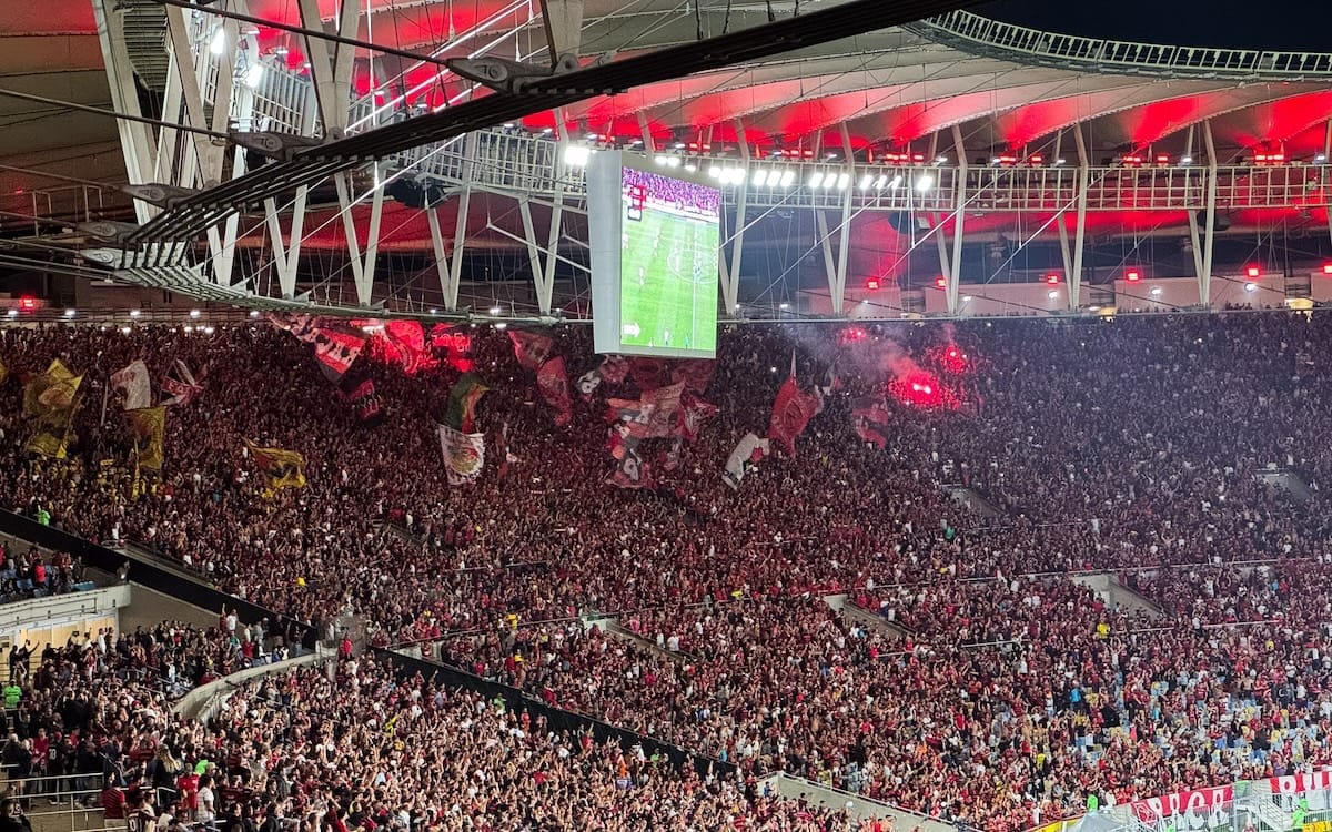Massive Flamengo crowd waving flags and lighting flares at Maracanã Stadium.