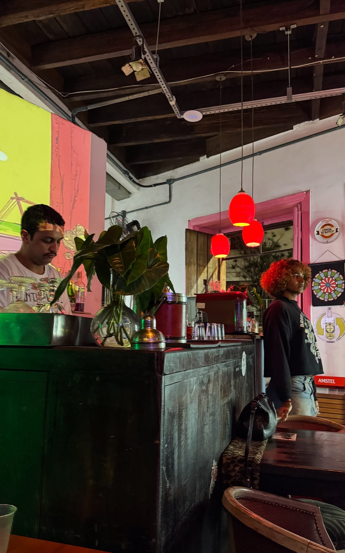 Bartender mixing drinks under warm red pendant lights in Bar Novooeste, known for its creative, artsy vibe.
