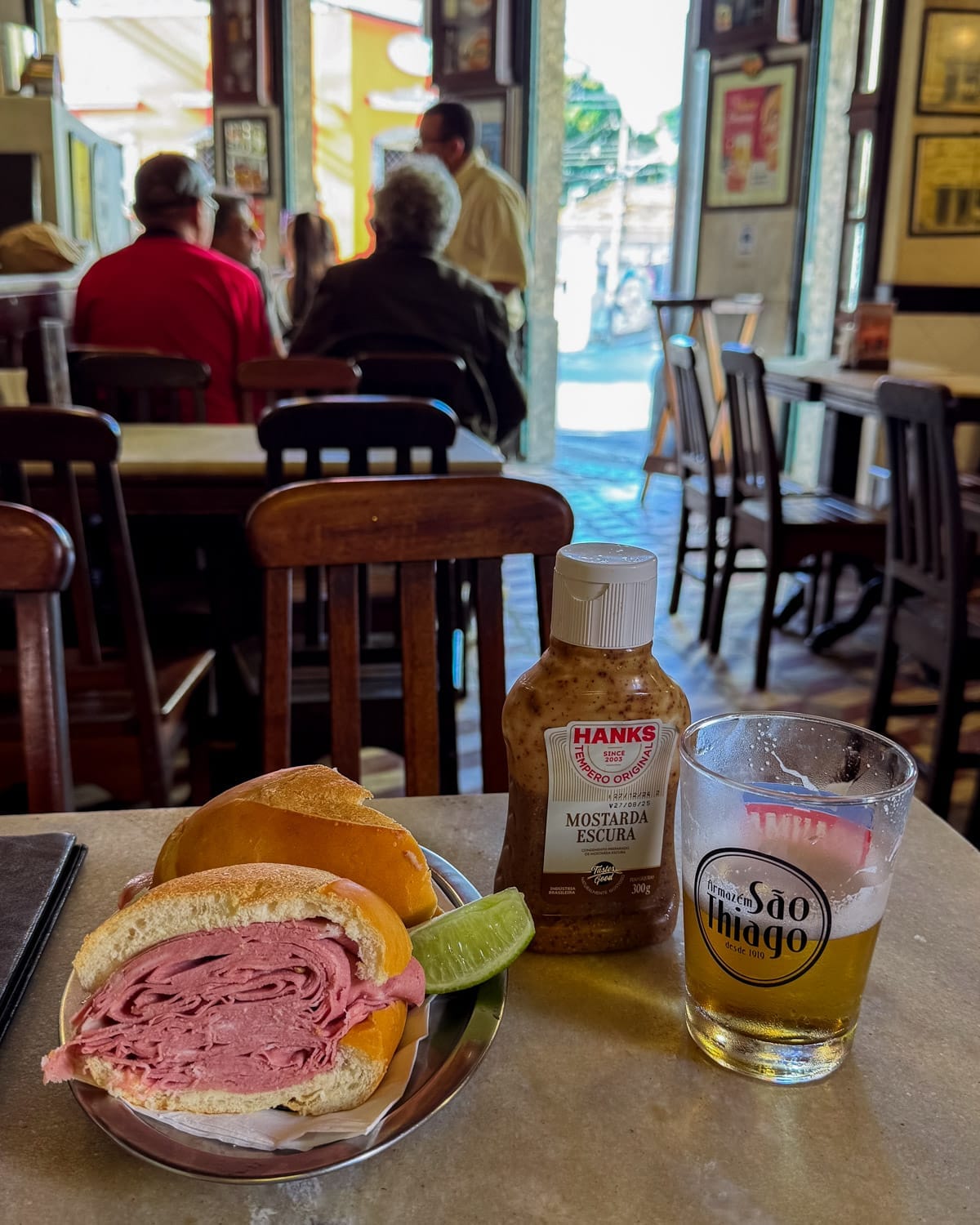 Classic Rio lunch of a mortadella sandwich with lime wedge, dark mustard, and cold draught beer inside the traditional bodega, Armazem Sao Thiago.