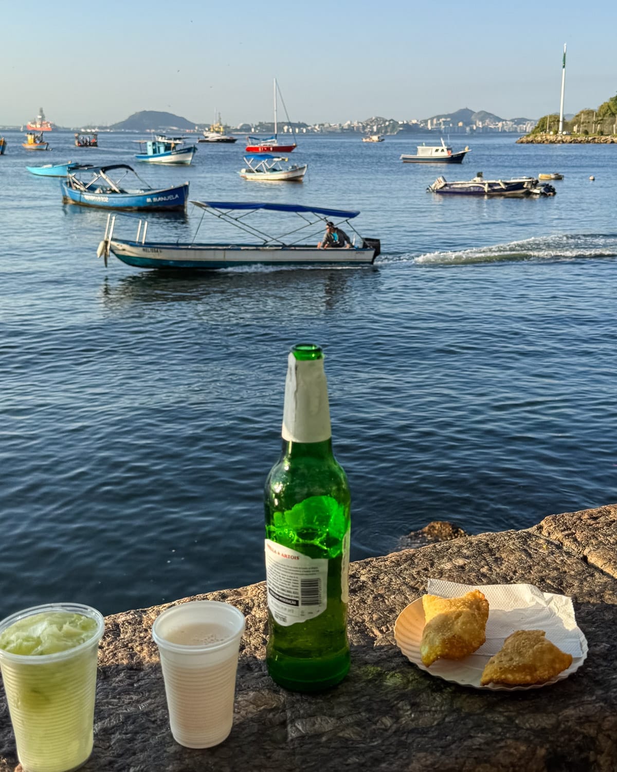 Cold drinks and pastéis by the waterfront at Bar Urca with fishing boats drifting by, a relaxed local hangout away from tourist crowds.