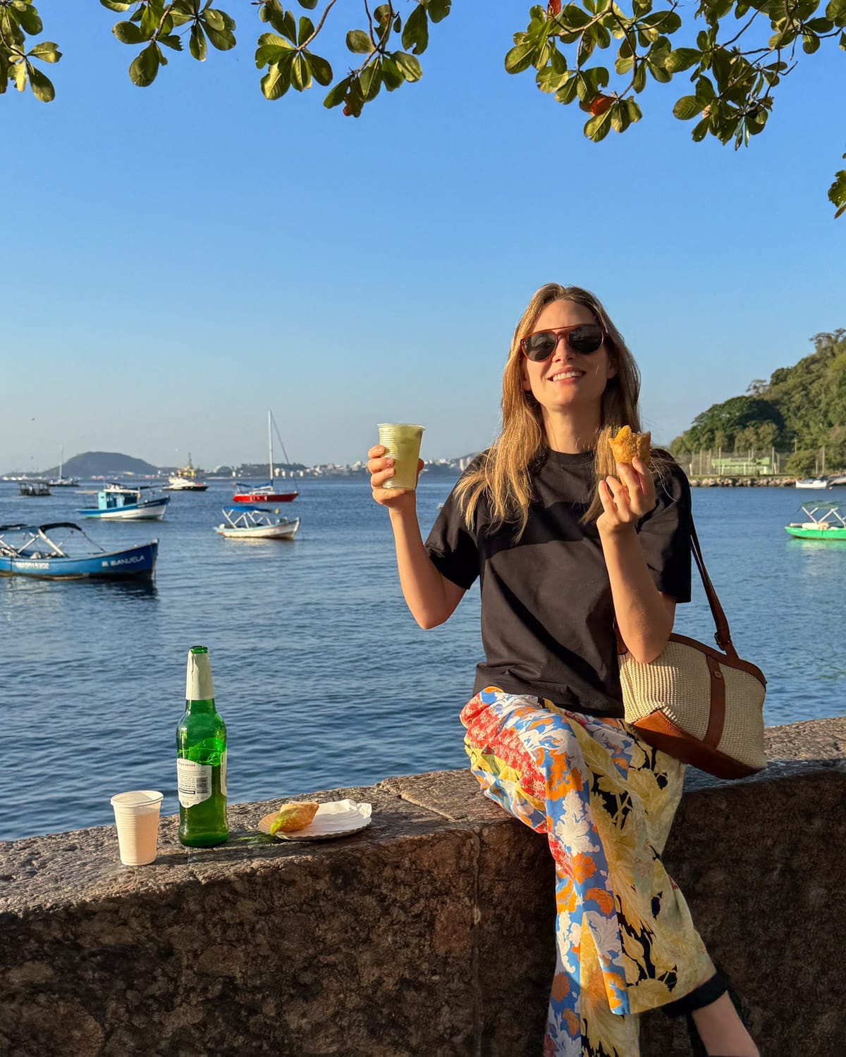 Cec sitting at sunset on a railing with a caipirinha and a purse with no designer logos.