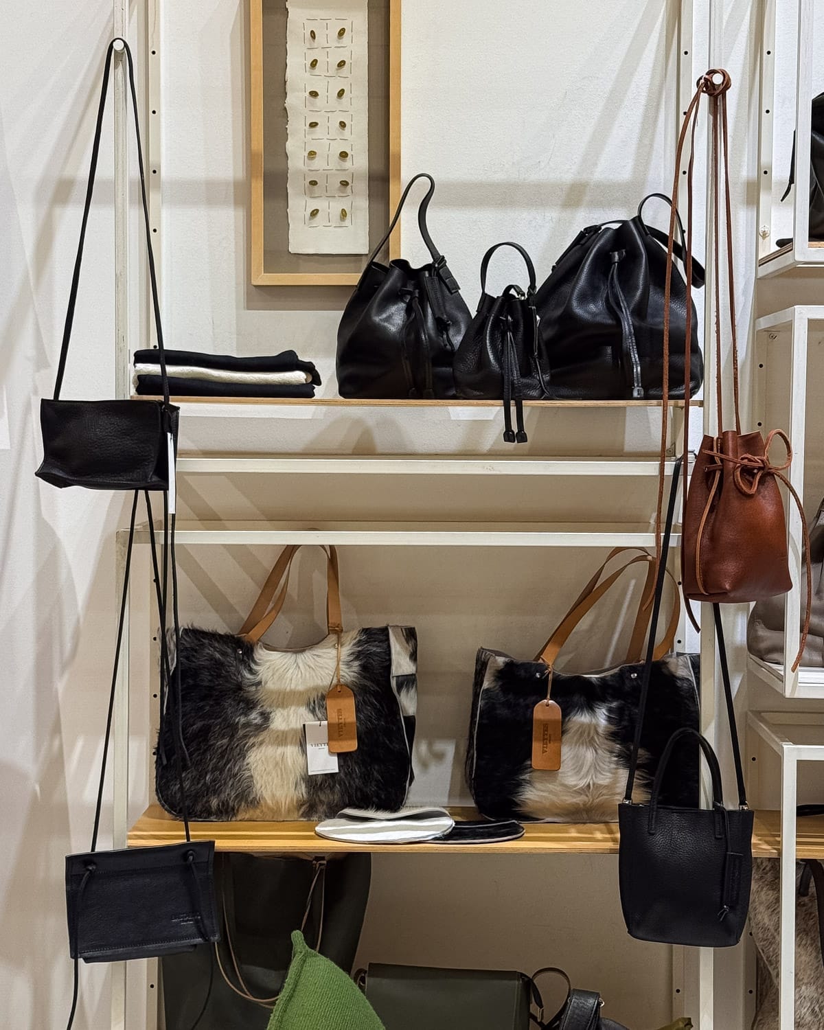 Shelf of Argentine leather bags, including black satchels and cowhide totes with tan handles at Tienda Patron.
