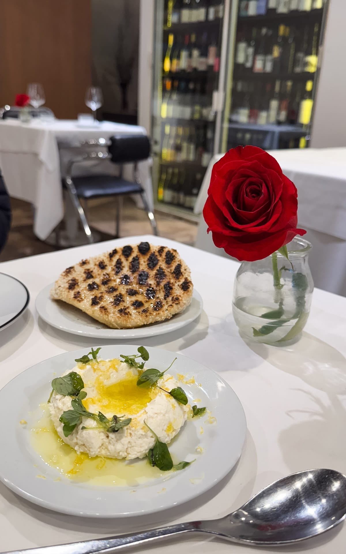 Plate of smoked ricotta cheese drizzled with olive oil and herbs, served with grilled sesame flatbread and a red rose on the table at Anafe restaurant.