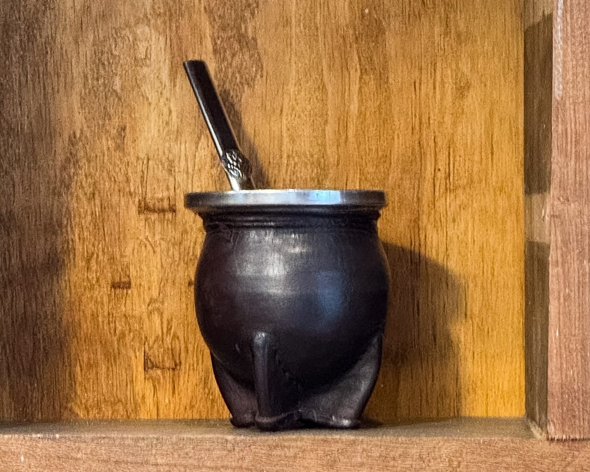 Traditional Argentine mate gourd with a metal straw on a wooden shelf.