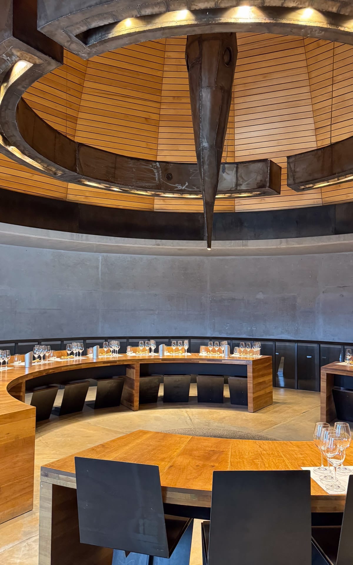 A circular tasting room at Bodega Zuccardi Valle de Uco with sleek wood tables set with rows of wine glasses beneath a dramatic pointed ceiling feature.