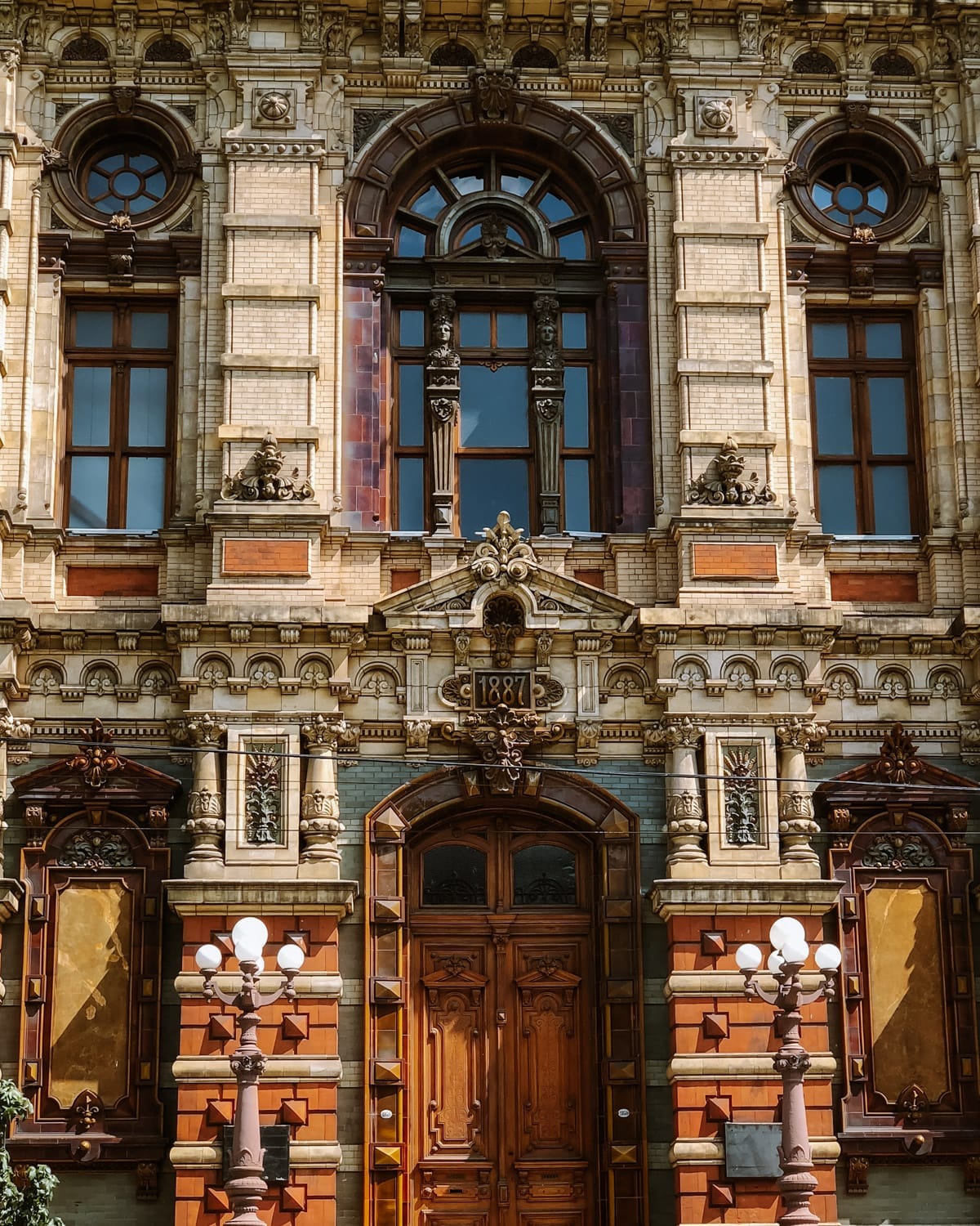 The ornate facade of an 1887 building, with arched windows, carved details, and rich wooden doors framed by decorative stonework in Buenos Aires.