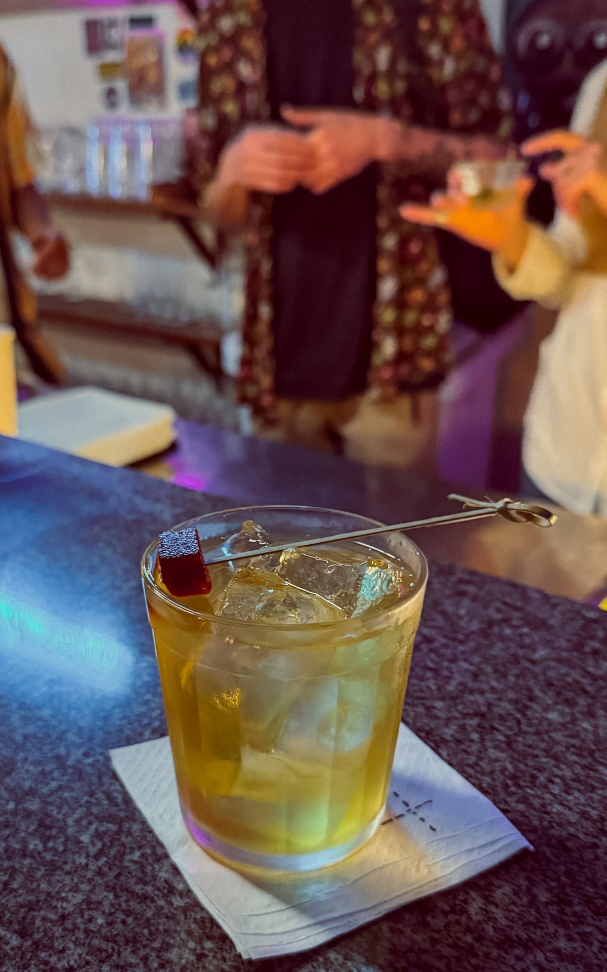 Handcrafted cocktail with clear ice and a garnish cube on a bar counter at Quartinho Bar, a local nightlife spot.