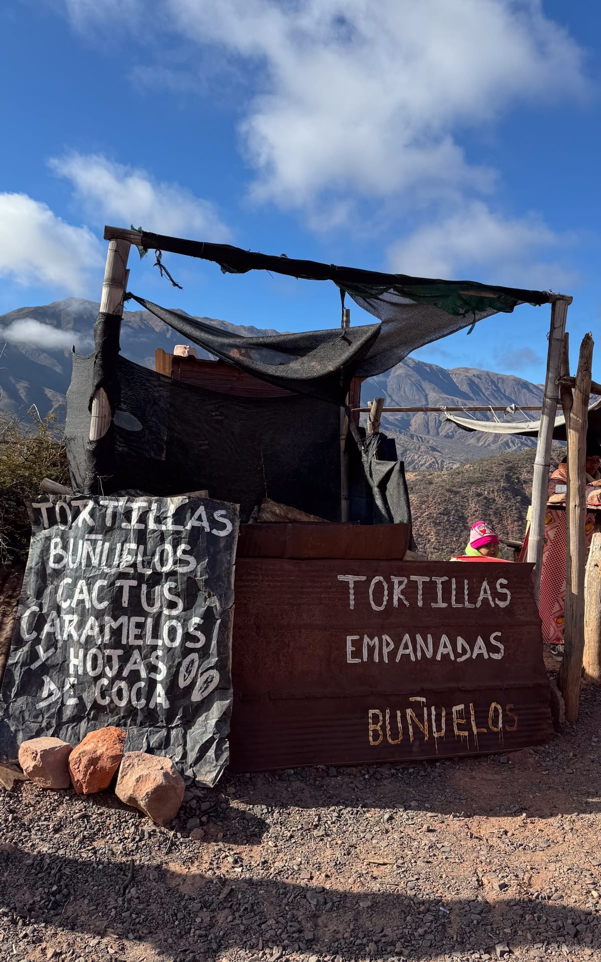 Rustic food shack along the mountain road selling tortillas, empanadas, and buñuelos with handwritten signs.