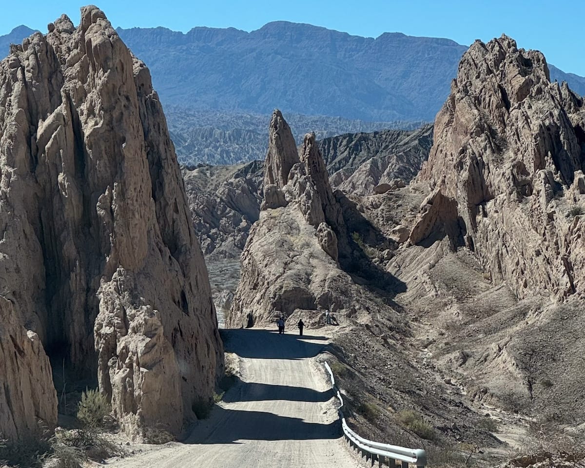 Dusty desert road weaving between sharp sandstone peaks and ridges in Salta Province’s Quebrada de las Flechas.