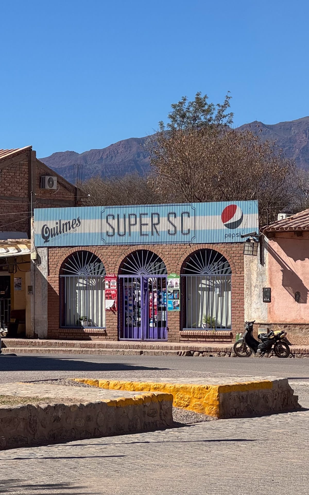 Colourful brick storefront with blue metal arches, Pepsi logo and mountain backdrop in the small village of San Carlos, Argentina.