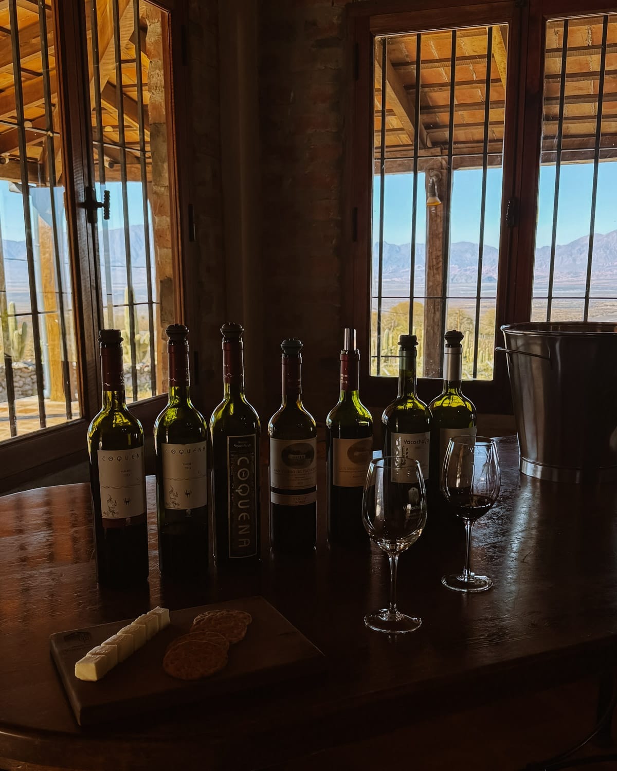 Bottles of high-altitude wine and cheese set on a wooden table overlooking the Andes at Yacochuya Winery.