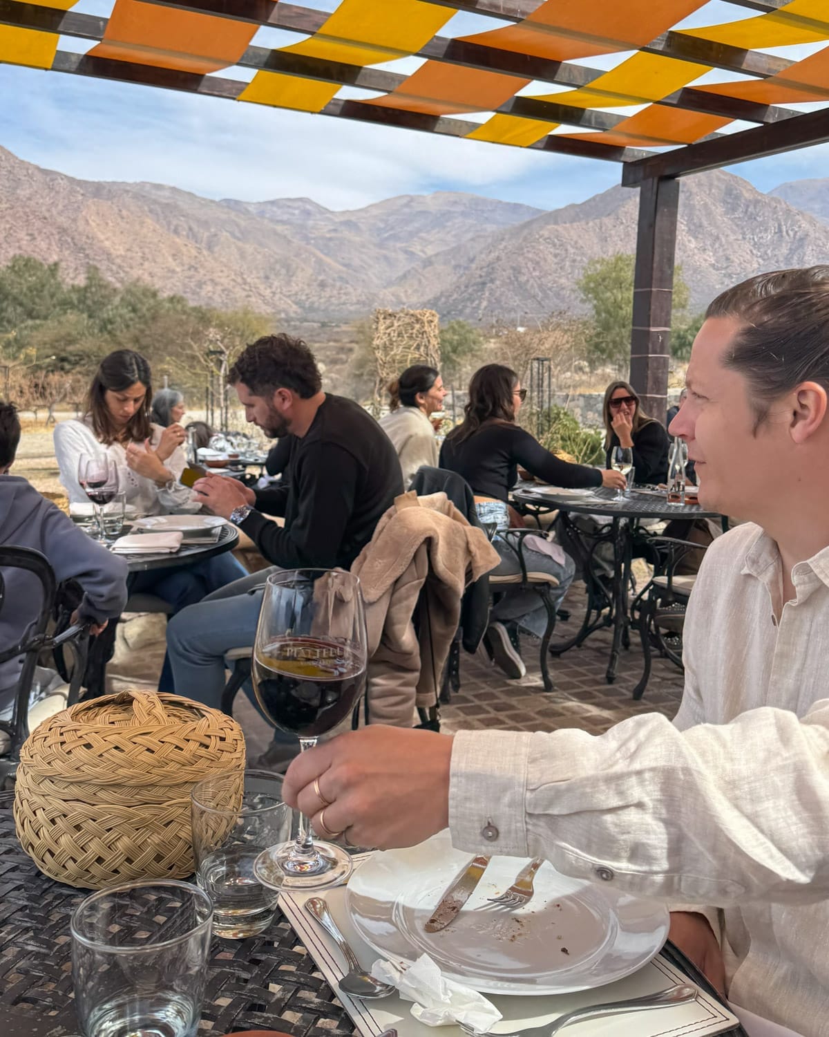 People dining outdoors at Piattelli Vineyards with glasses of Malbec and mountain views in the background.