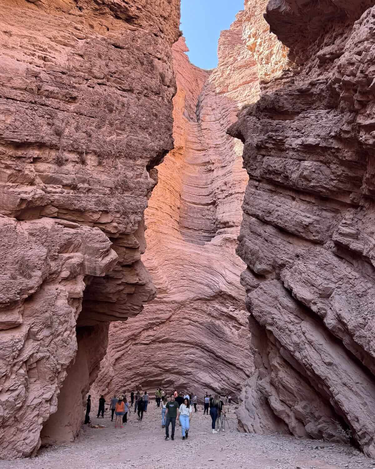 Visitors walking between towering red rock walls at The Amphitheatre in Quebrada de las Conchas, Salta Province.